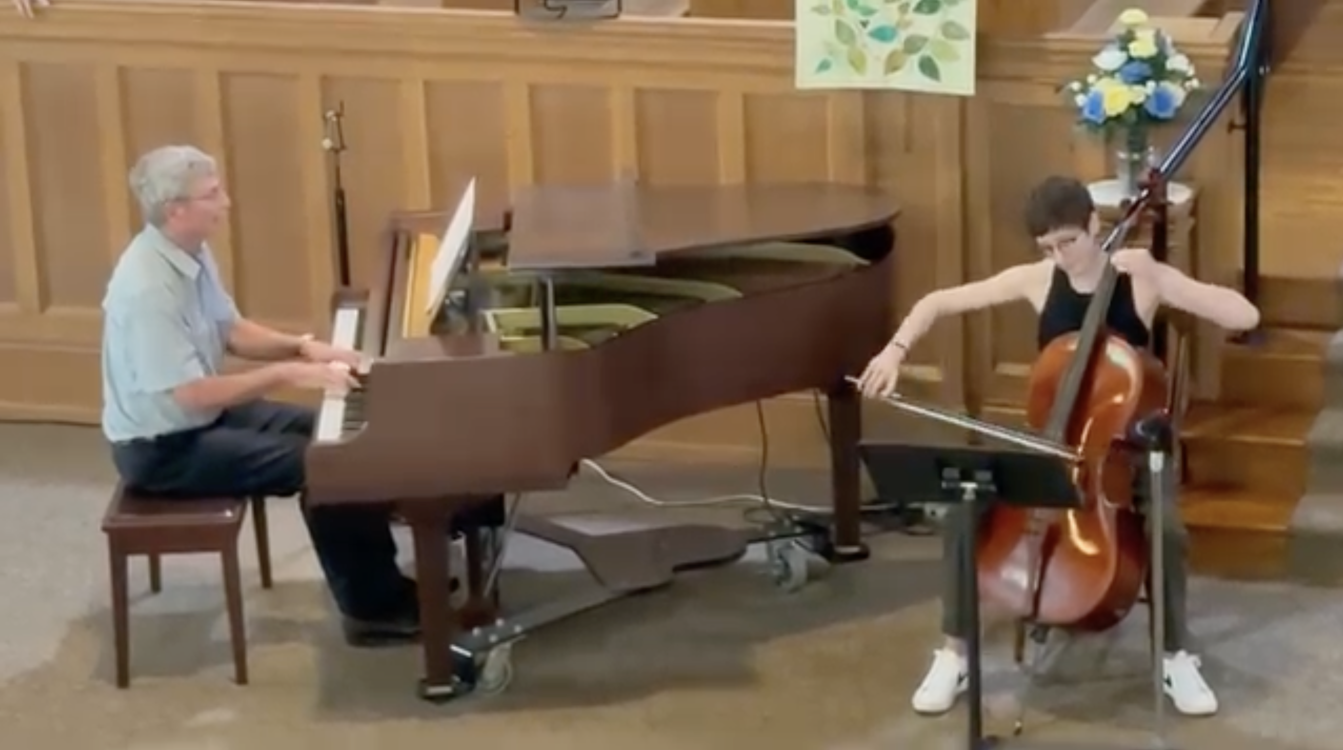 A man plays piano and a woman plays with him on cello.