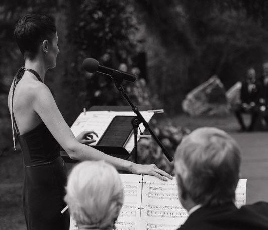 A woman in formal wear stands in front of a microphone.